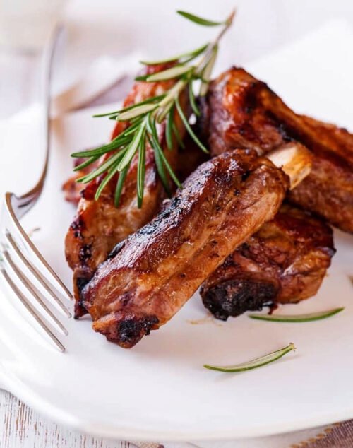 Costillas de cerdo glaseadas y asadas servidas en un plato blanco con romero