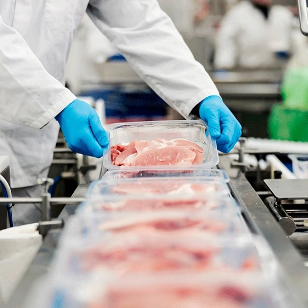 Operarios envasando bandejas de carne en una línea de producción