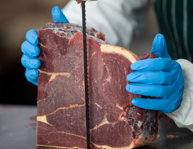 Operario cortando una pieza de carne con una sierra de cinta